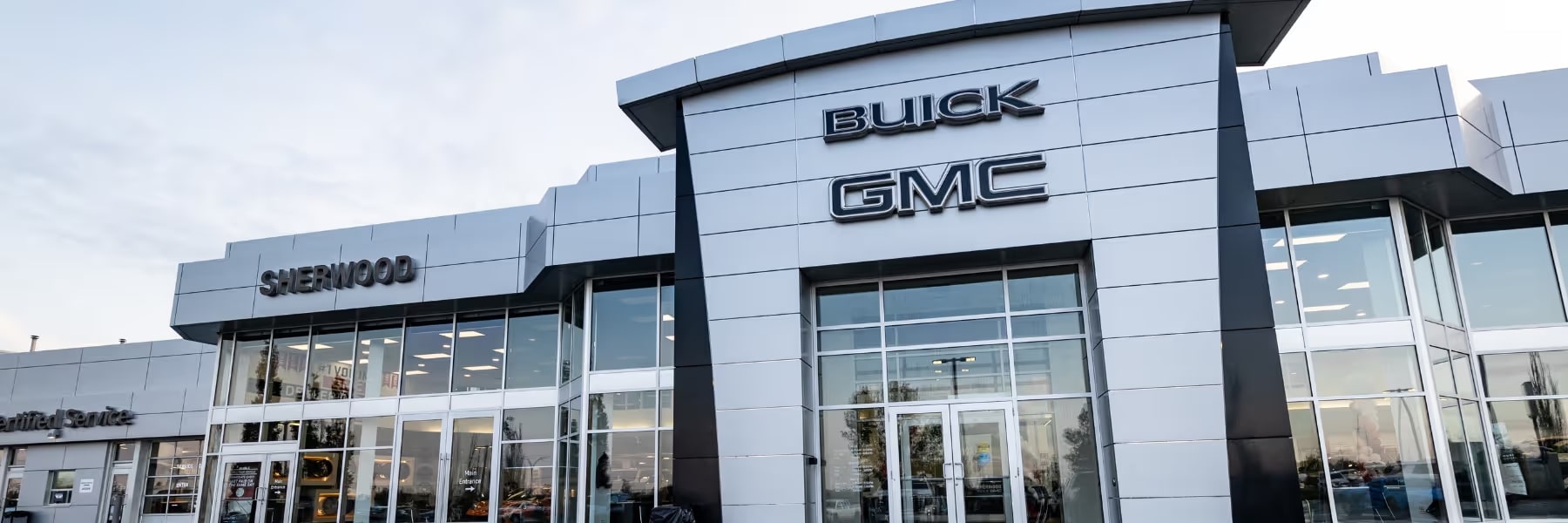 Exterior view of Sherwood Buick GMC dealership showcasing modern architecture and signage. The sleek building features large glass windows and a prominent display of the Buick and GMC logos, highlighting automotive sales and services.