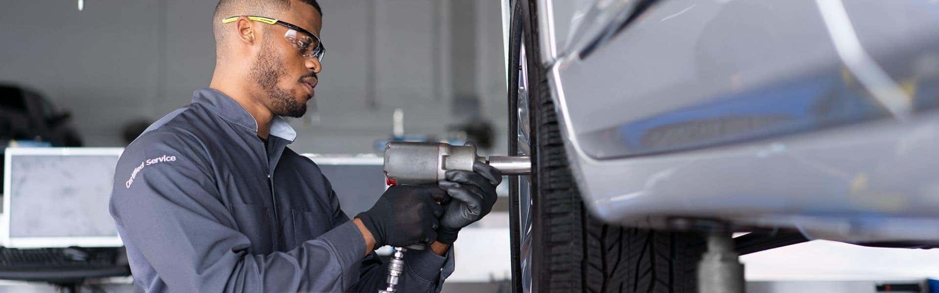 Automotive technician using a power tool to perform tire maintenance in a service garage, wearing safety glasses and gloves for protection, showcasing professional car repair services.