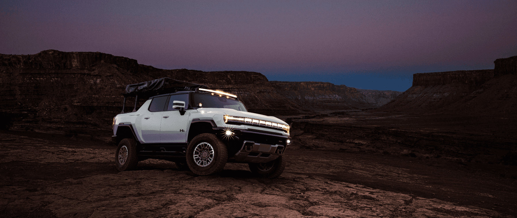 Electric Hummer EV parked on rocky terrain at dusk, showcasing its rugged design and off-road capabilities against a dramatic landscape.