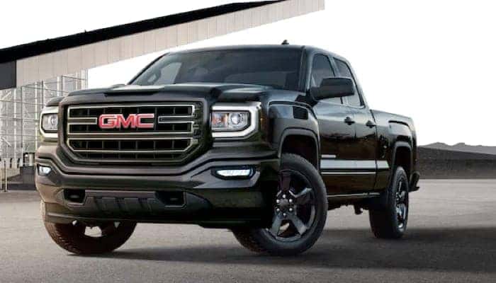 Black GMC truck parked in front of a modern building, showcasing its bold design and sleek exterior features. Ideal for those seeking a combination of style and rugged performance.