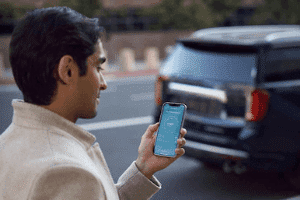 Young man using a smartphone app for car services, standing near a parked vehicle on a city street.