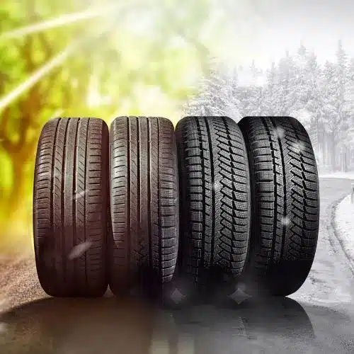 Four car tires displayed side by side, showcasing different tread designs for various weather conditions: summer, all-season, and winter tires. The background transitions from a sunny landscape to a snowy road, highlighting the importance of choosing the right tires for safety and performance.