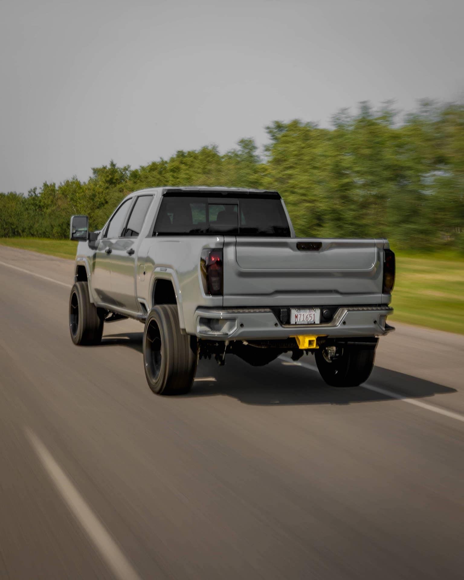 Silver pickup truck with custom wheels driving on a rural road surrounded by greenery, showcasing robust design and performance.