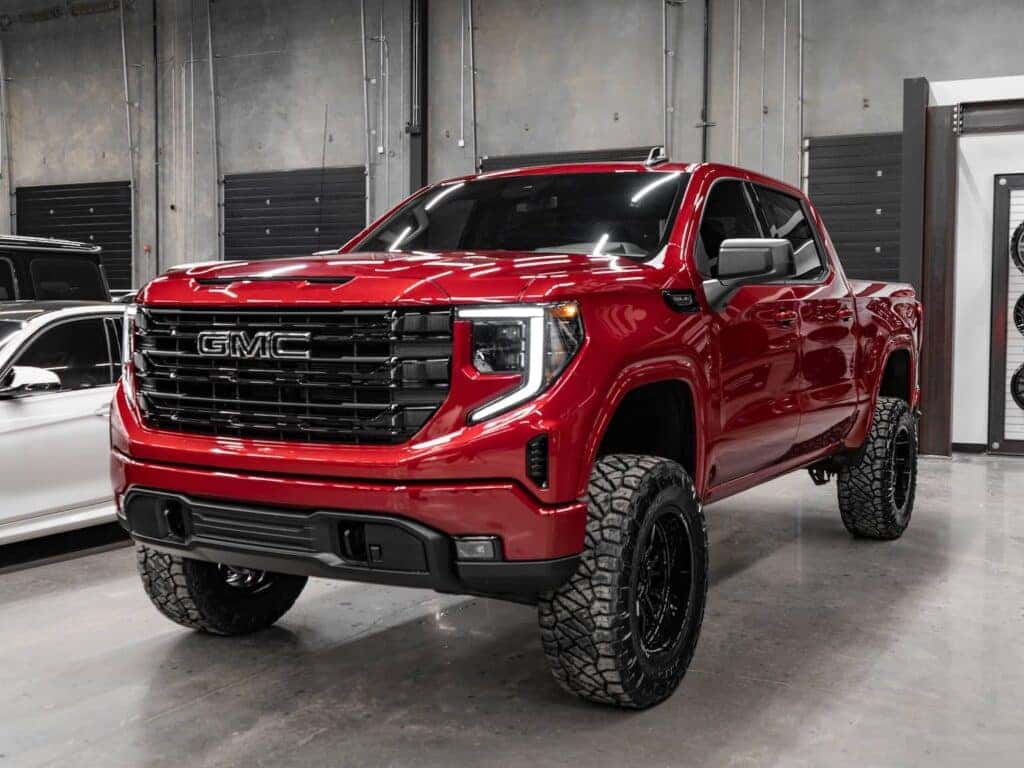 GMC Sierra truck in vibrant red color, parked indoors showcasing its bold design, lifted suspension, and rugged tires, emphasizing strength and performance.