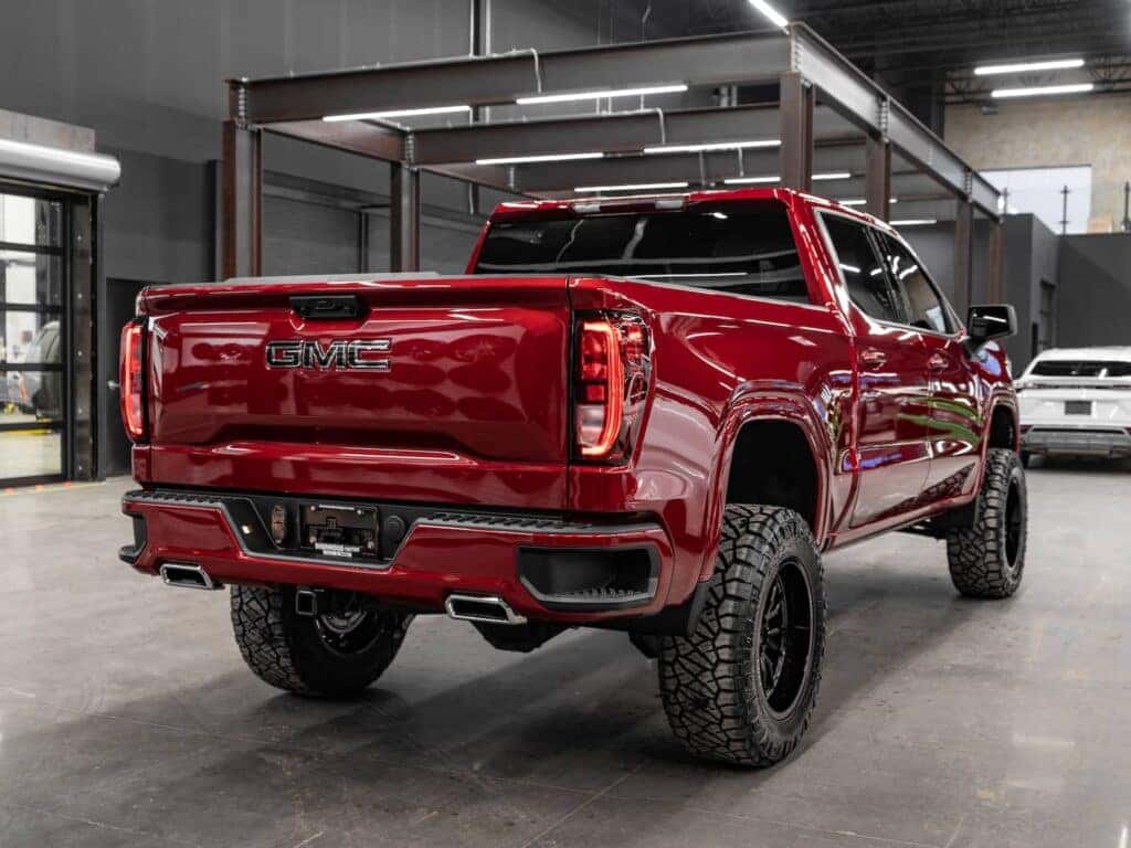 Red GMC pickup truck with off-road tires showcased in a modern garage setting, highlighting its robust design and custom features.