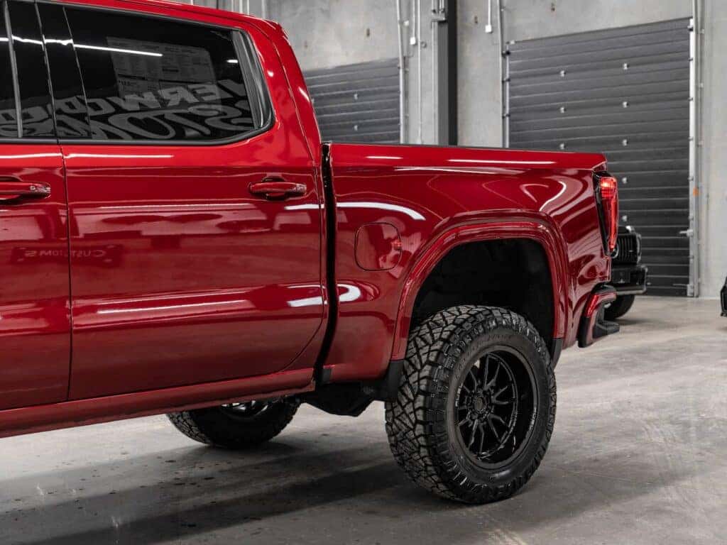 Close-up view of a red pickup truck showcasing the rear wheel, rugged black tires, and polished bodywork, set against a modern garage background. Ideal for automotive enthusiasts and truck customization showcases.