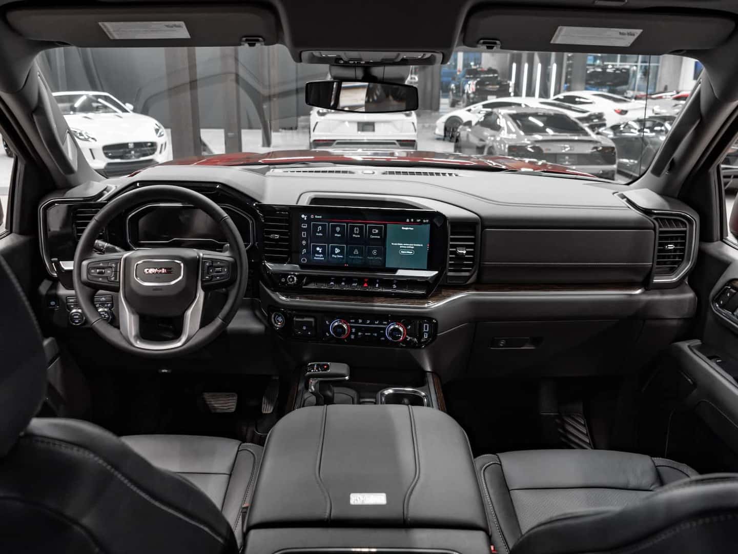 Interior view of a modern GMC pickup truck showcasing the stylish dashboard, large touchscreen display, and comfortable black leather seating, with luxury details highlighted in a sleek automotive showroom.