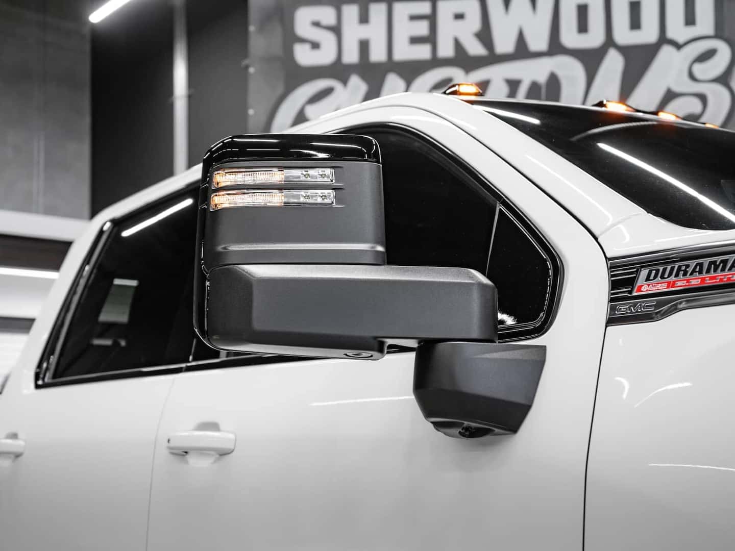 Close-up of a white GMC truck featuring a side mirror with integrated LED turn signals, showcasing modern design elements and details suitable for truck enthusiasts and automotive enthusiasts.