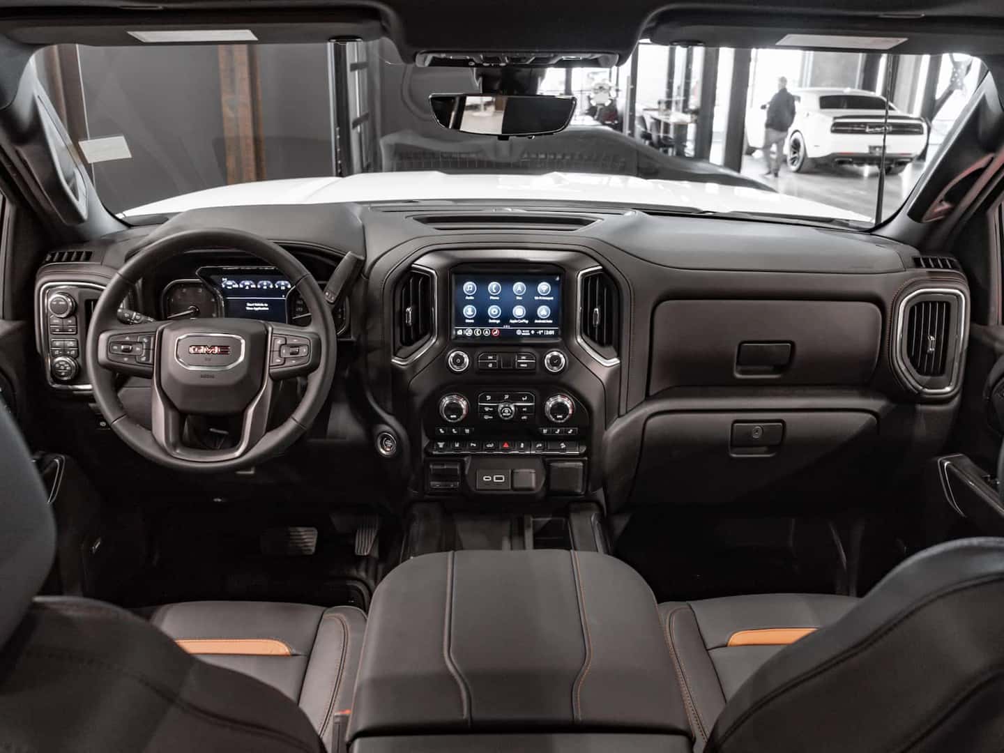 Interior view of a modern GMC truck showcasing a sleek dashboard, advanced touchscreen display, steering wheel controls, and premium leather seating, emphasizing comfort and technology.