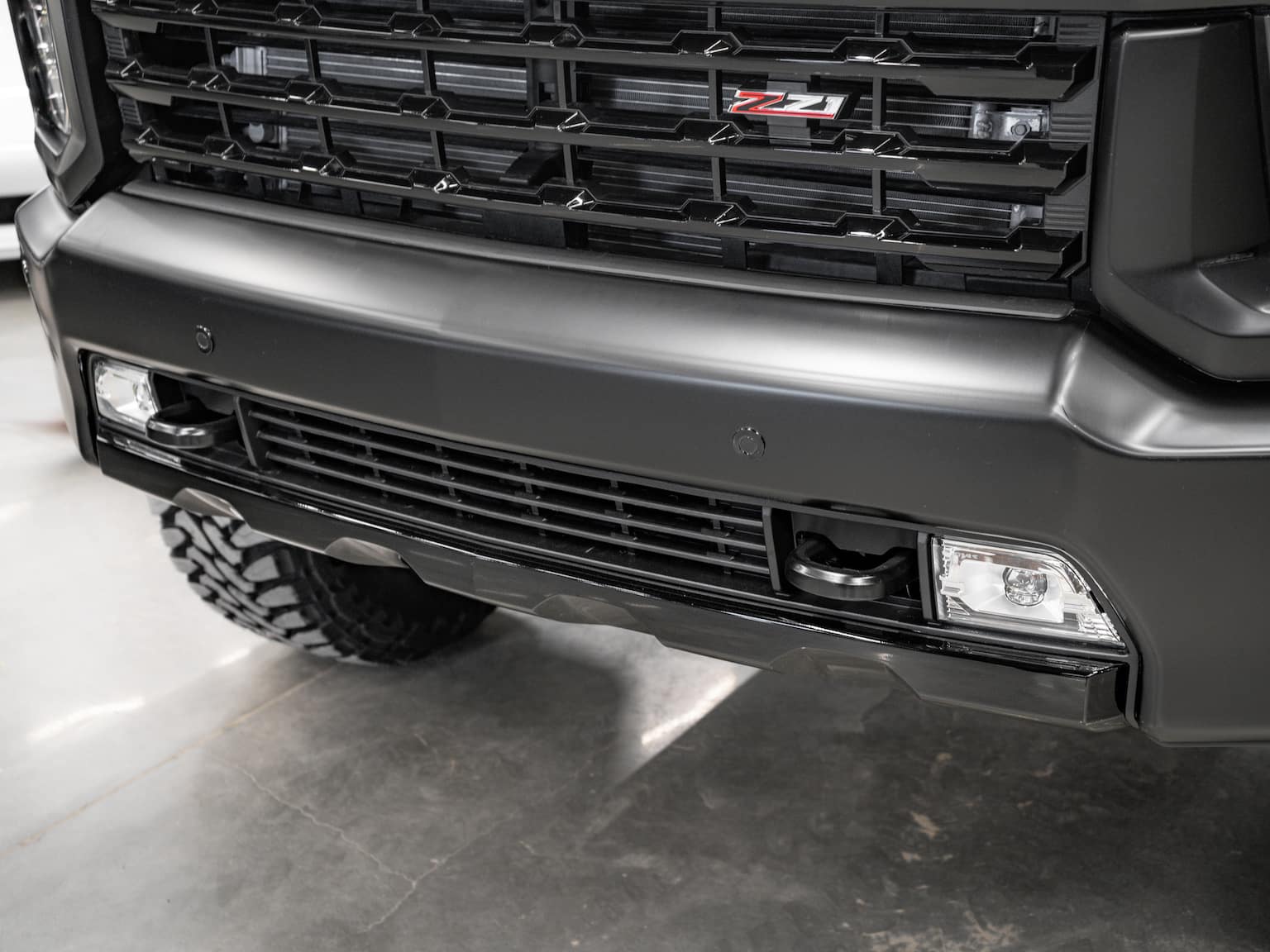 Front view of a black truck showcasing the aggressive grille, sleek bumper design, and integrated fog lights, highlighting its robust and modern styling ideal for off-road capabilities.