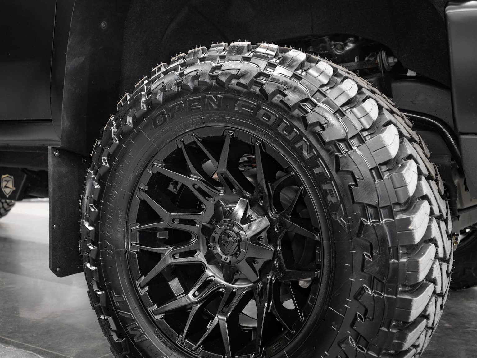 Close-up of a black off-road tire with a rugged tread pattern mounted on a stylish black alloy wheel, showcasing the Open Country brand, designed for enhanced traction and durability on rough terrains.