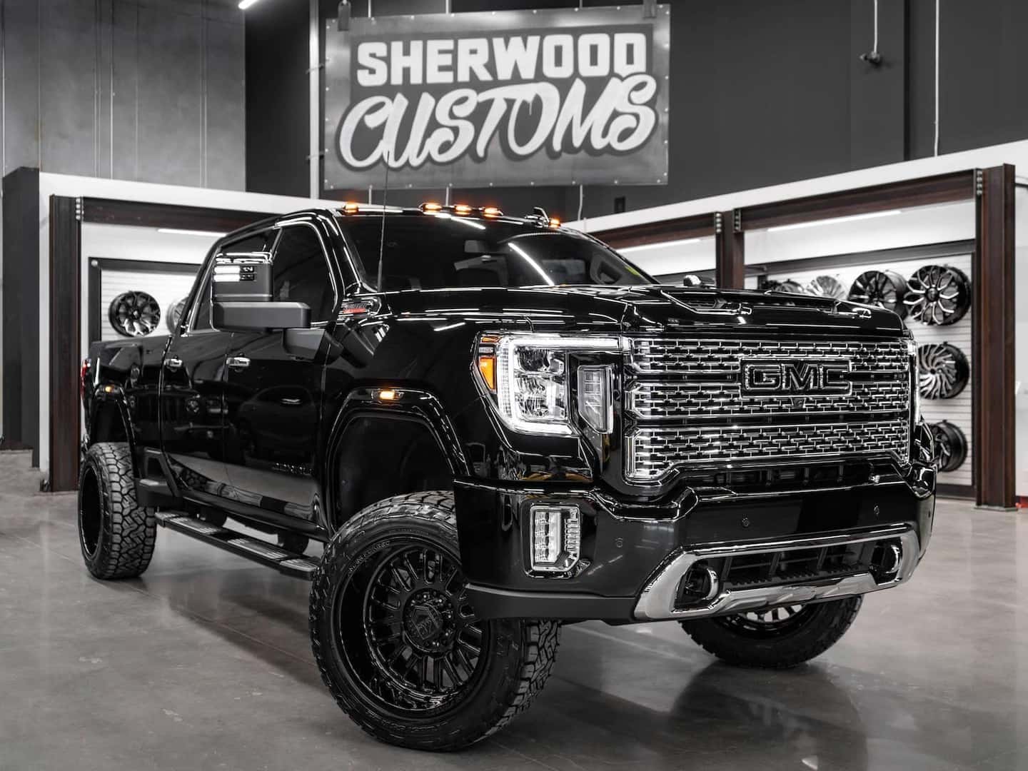 Custom black GMC truck displayed at Sherwood Customs showroom, featuring upgraded wheels and enhanced suspension for a rugged look.