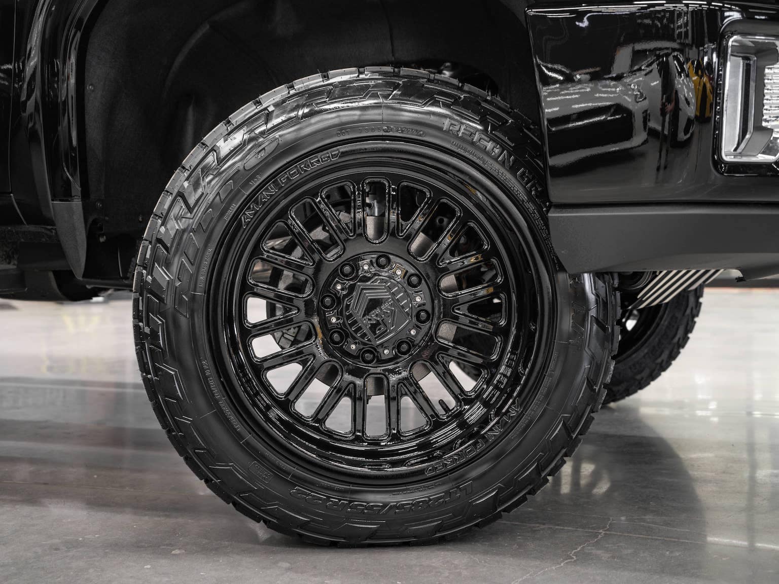 Close-up view of a black off-road tire mounted on a vehicle, showcasing a stylish alloy wheel design with detailed spokes and aggressive tread pattern, highlighting its suitability for rugged terrains and improved vehicle performance.