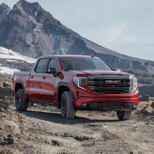 Black GMC Sierra truck parked in a modern landscape with wooden architecture and greenery, showcasing its sleek design and premium features.