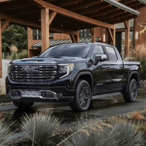Black GMC Sierra truck parked in a modern landscape with wooden architecture and greenery, showcasing its sleek design and premium features.
