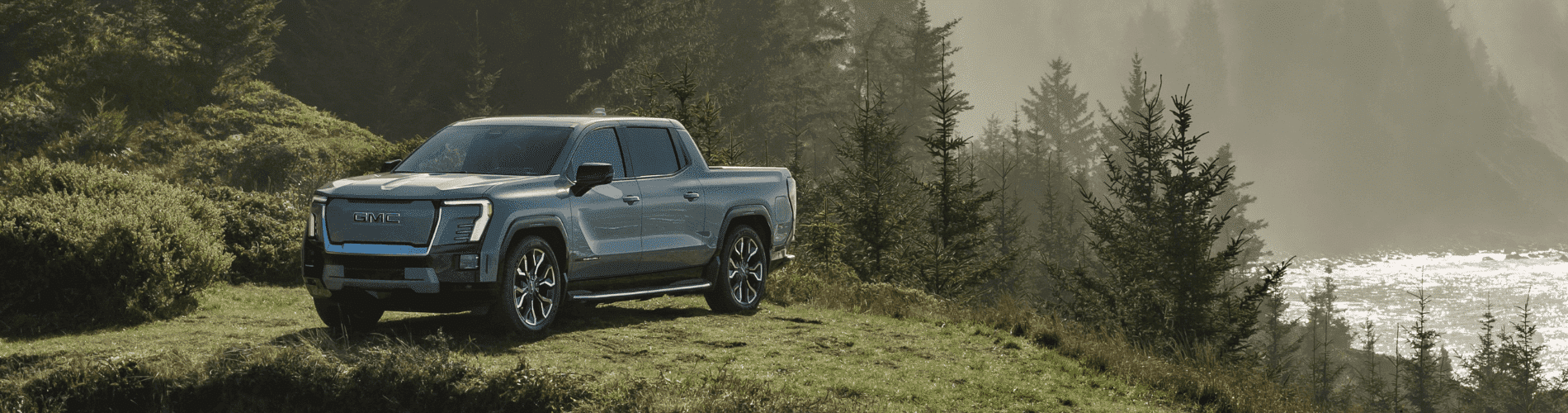 GMC electric pickup truck parked in a scenic landscape with lush greenery and distant ocean views, showcasing its modern design and rugged appeal for outdoor adventures.