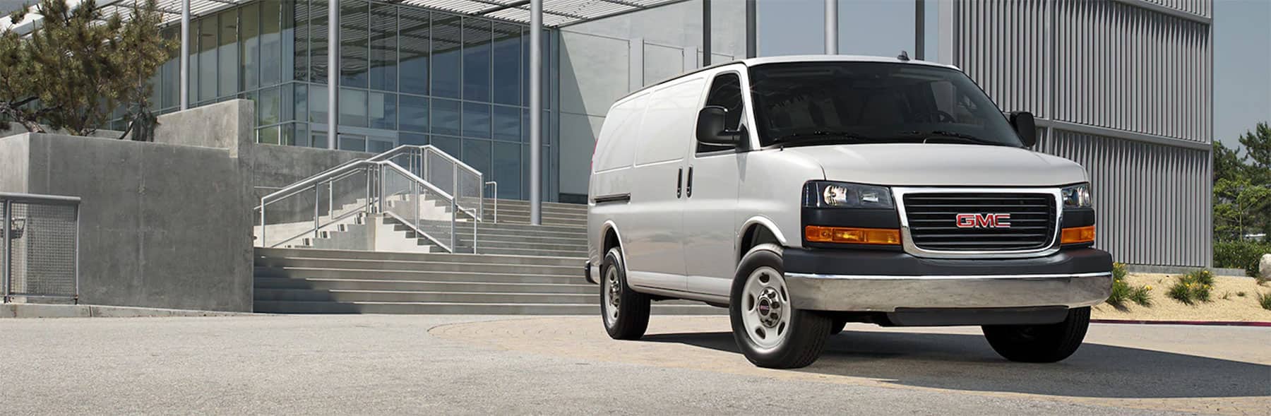GMC cargo van parked in front of a modern building with large glass windows, showcasing its sleek design and functionality for commercial use.