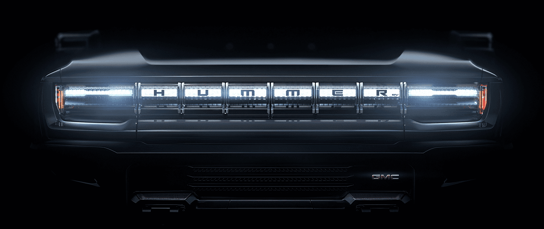 Front view of a GMC Hummer EV showcasing its illuminated grille and distinctive branding, highlighting its modern electric design and rugged features against a dark background.