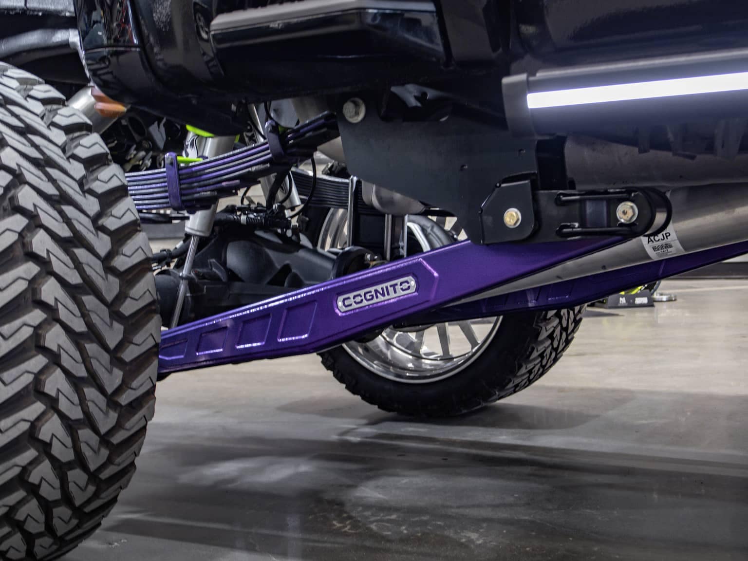 Close-up view of a purple CGS Nitro suspension component on a modified truck, highlighting the robust design and off-road capabilities, with a focus on the large tire and intricate underbody mechanics.