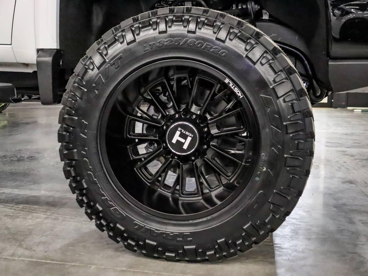 Black alloy wheel with a rugged tire designed for off-road performance, featuring an LT325/60R20 size and aggressive tread pattern. Ideal for enhancing traction and stability in various terrains.