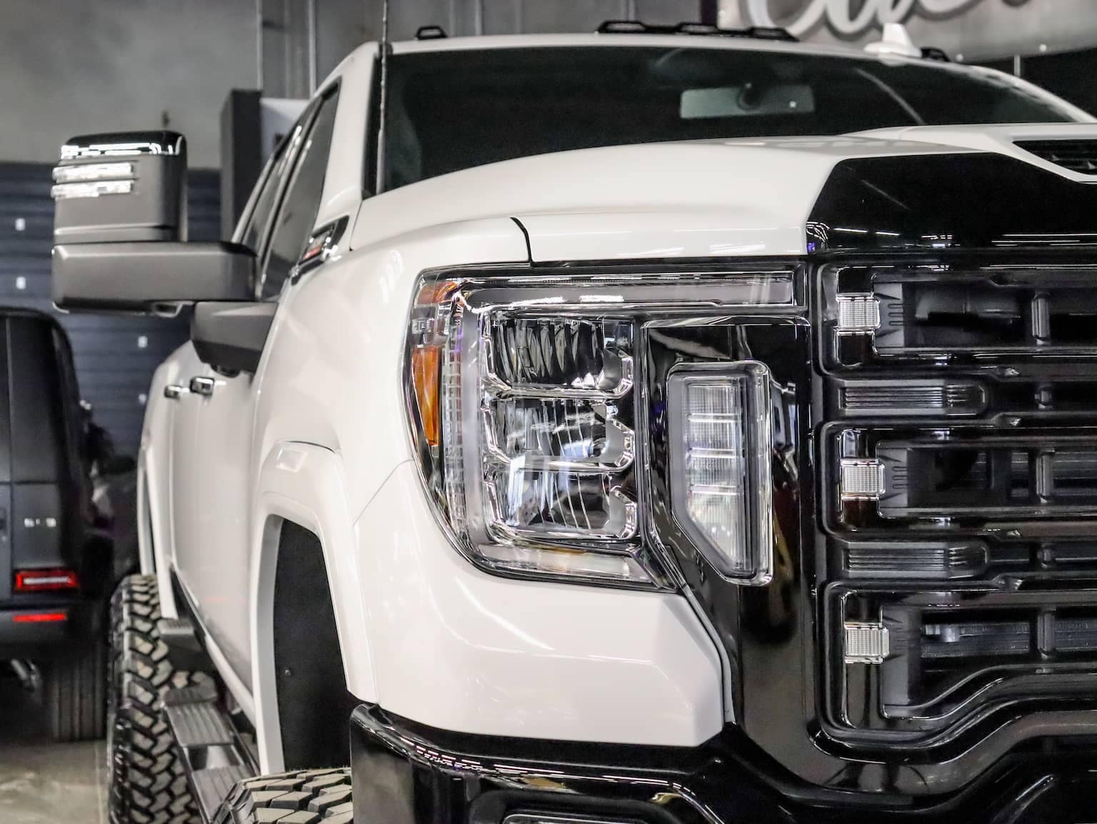 Close-up of a white pickup truck showcasing its bold front grille, modern headlights, and reflective side mirror, emphasizing its robust design and off-road capabilities. Ideal for truck enthusiasts and potential buyers looking for performance vehicles.