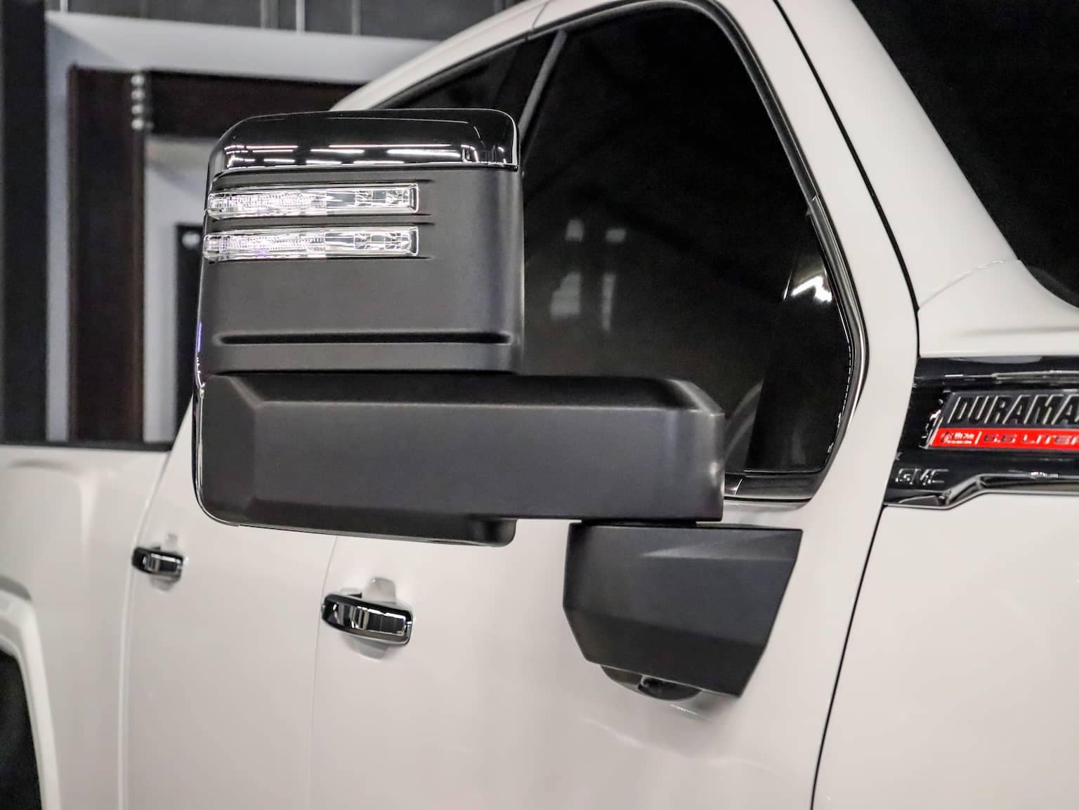 Close-up view of a white pickup truck's side mirror featuring LED turn signals and a sleek black design, showcasing modern automotive styling and functionality.