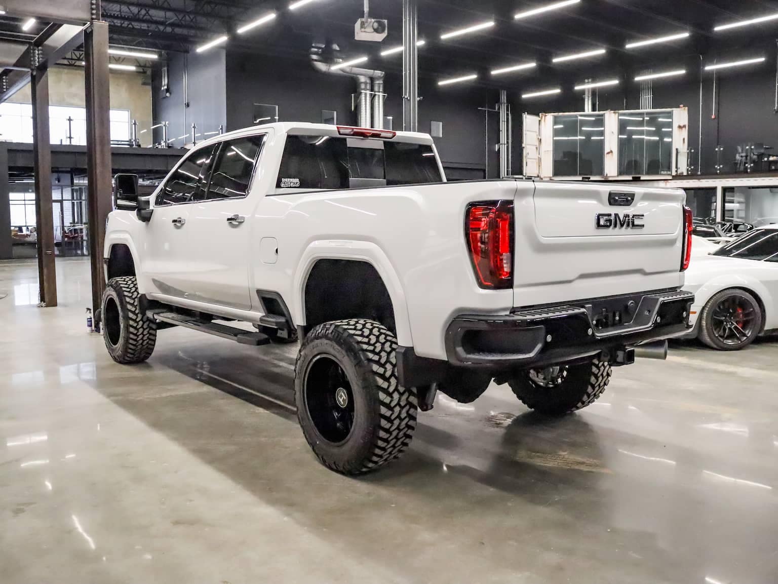 White GMC truck with off-road tires showcased indoors, highlighting its rugged design and spacious interior.