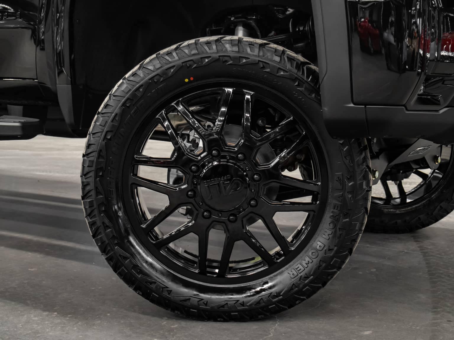 Close-up view of a black off-road truck tire with an intricate six-spoke rim design. The tire features a rugged tread pattern for enhanced grip and performance, emphasizing durability and style. Ideal for off-road enthusiasts and vehicle customization.