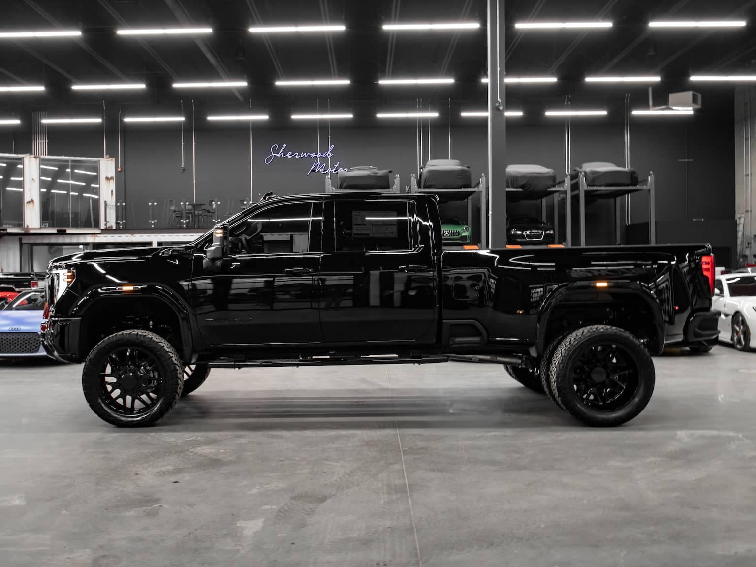 Black lifted pickup truck displayed in a modern showroom with a sleek design and oversized black wheels, showcasing its rugged capabilities and stylish appearance.