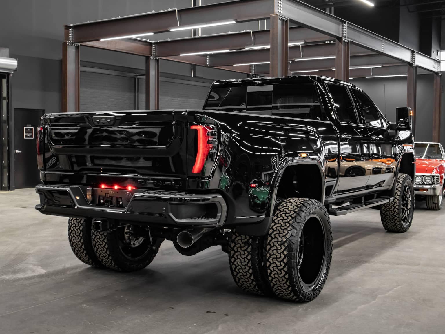 Black lifted pickup truck with oversized tires displayed in a modern showroom, showcasing a sleek design and powerful presence, highlighting its robust rear lights and chrome accents.