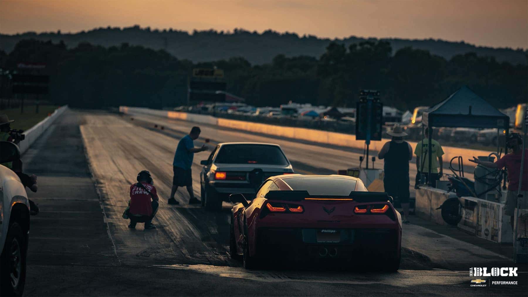 Black muscle car performing a burnout on a racing track, generating smoke and showcasing its powerful rear-wheel drive capabilities. The vehicle features stylish alloy wheels and an aerodynamic body, emphasizing its performance-focused design.