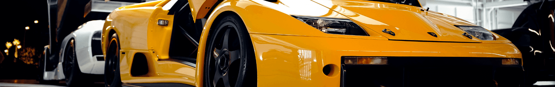 Close-up of a striking yellow sports car showcasing its sleek design and aerodynamic features, parked alongside a white vehicle in a well-lit garage setting. Highlights include distinctive headlights and open doors, emphasizing its modern aesthetics and performance-oriented build.