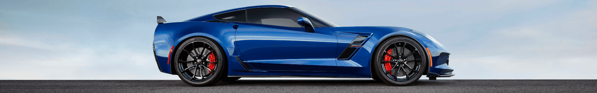 Blue sports car parked on a racetrack, showcasing sleek aerodynamic design, black alloy wheels, and red brake calipers against a cloudy sky backdrop.