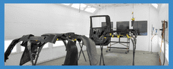Automotive chassis being painted in a specialized spray booth, featuring adjustable stands and an organized workspace designed for professional vehicle restoration.