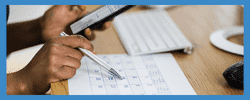 Person using a smartphone and writing on a calendar while managing tasks at a desk, highlighting productivity and organization.