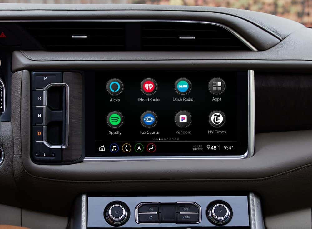 Dashboard display featuring a modern infotainment system with various app icons including Alexa, iHeartRadio, Spotify, Fox Sports, Pandora, and NY Times, indicating connectivity and entertainment options for drivers.