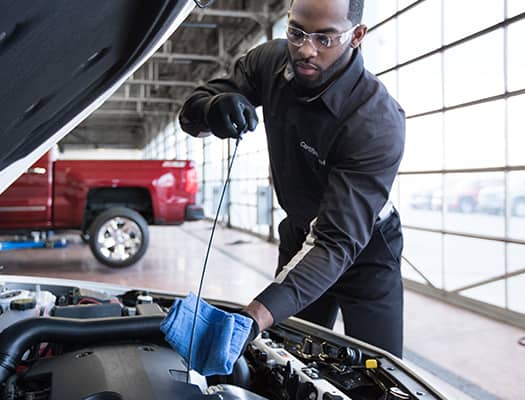 Automotive technician performing an oil check under the hood of a car in a well-lit garage, showcasing vehicle maintenance skills and attention to detail.