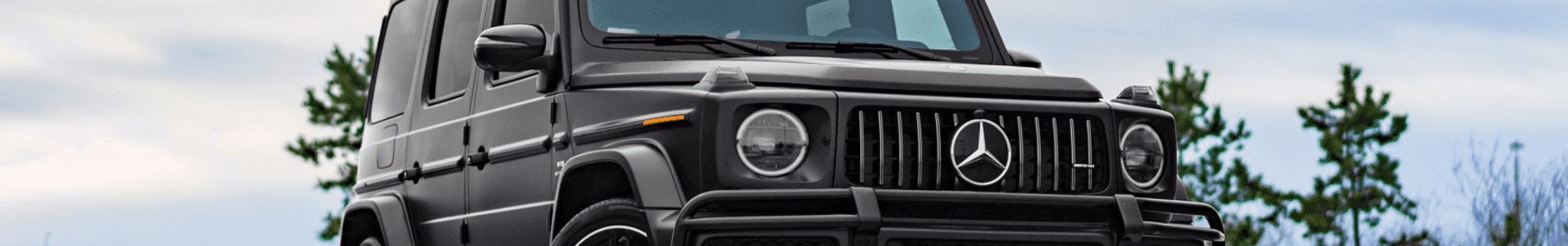 Black Mercedes-Benz G-Class SUV parked against a backdrop of trees and blue sky, highlighting its rugged design and luxury features.
