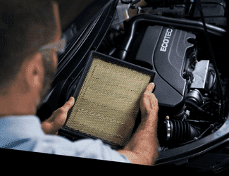A mechanic inspecting and replacing an air filter in a vehicle's engine compartment featuring an Ecotec engine.