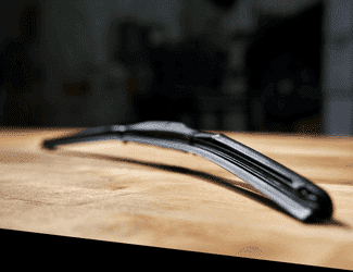 Close-up image of a black windshield wiper blade resting on a wooden surface, with a blurred background highlighting its design details and rubber edge. Ideal for auto parts or vehicle maintenance content.