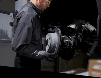 Mechanic inspecting and installing a brake rotor in an automotive workshop, demonstrating brake system maintenance and repair.