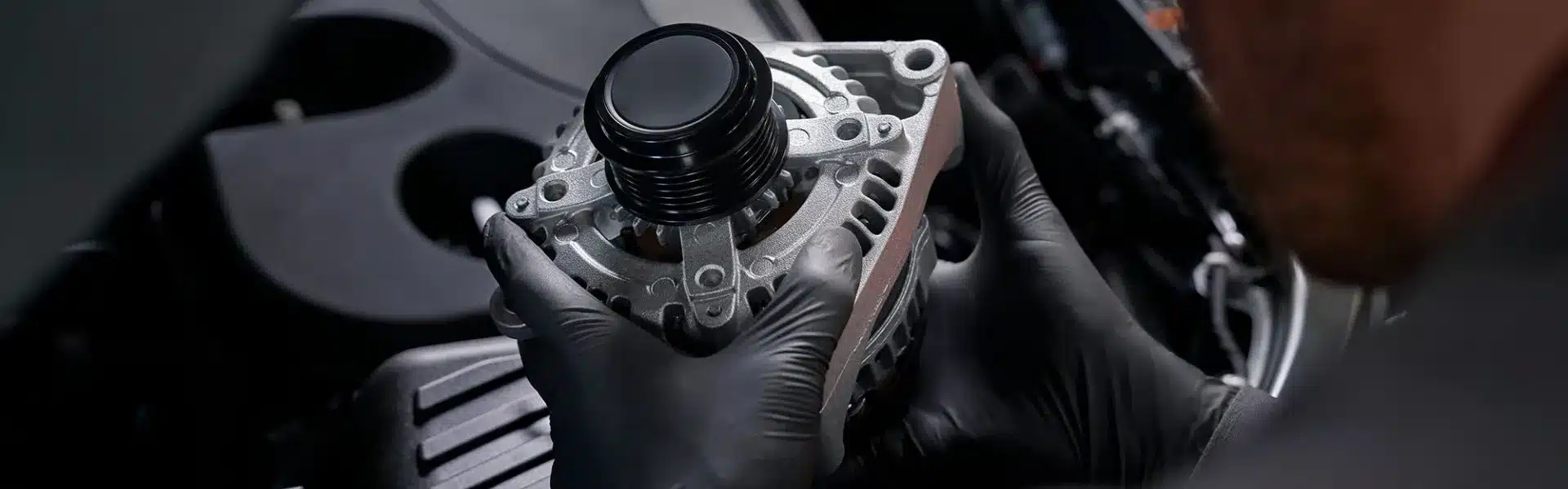 A mechanic holding a new alternator while performing maintenance on a car engine, wearing black gloves, focused on vehicle repair and electrical system upgrades.