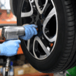 Worker using an impact wrench to tighten a wheel on a car in an automotive repair shop.