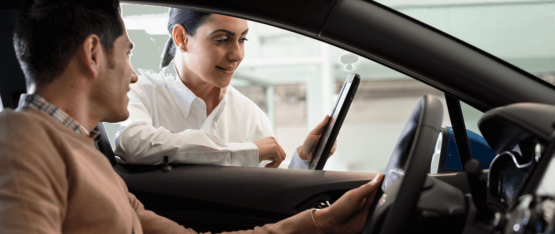 A customer in a car consulting with a sales representative holding a tablet, discussing features or services in an automotive setting.