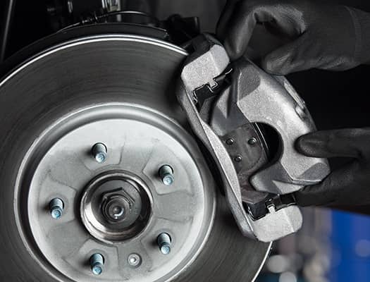 Close-up of a mechanic's hands installing a brake caliper onto a brake disc, showcasing the intricate components of automotive braking systems.