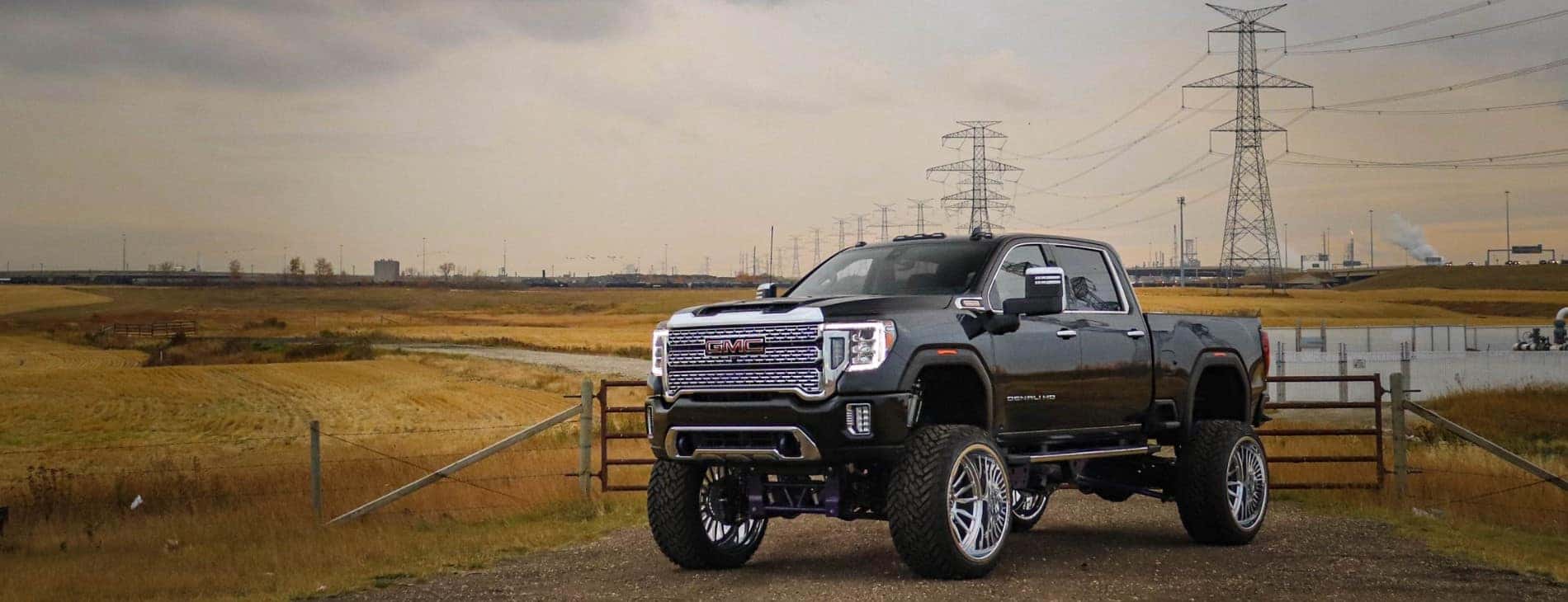 High-performance GMC truck parked in an open field with power lines in the background, showcasing its rugged design and lifted suspension for off-road capability.