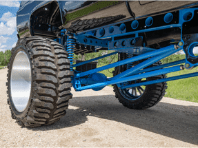 Close-up view of a lifted truck's suspension system, featuring prominent blue shock absorbers, control arms, and oversized off-road tires, highlighting its rugged design and enhanced performance capabilities.