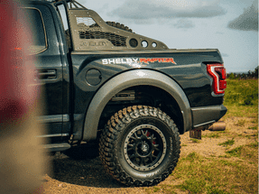 Shelby Raptor truck with oversized tires parked on a grassy field, showcasing its rugged exterior and custom design features.