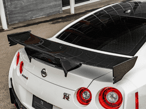 Close-up of the rear of a white Nissan GT-R with a prominent carbon fiber spoiler and distinctive circular taillights, highlighting its sporty design and performance features.