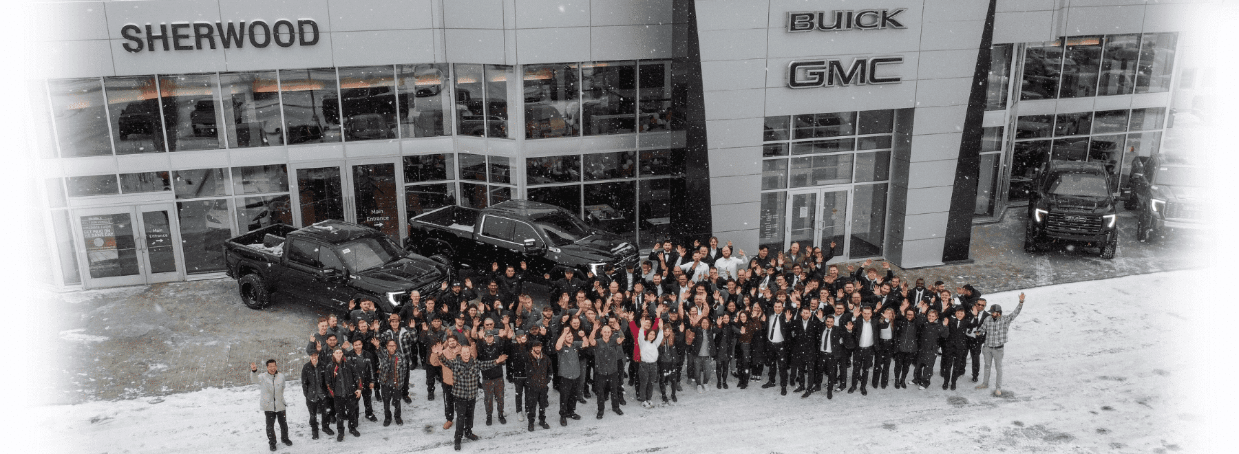 Group photo of Sherwood Buick GMC employees celebrating outside the dealership in snowy conditions, with several black GMC vehicles displayed prominently.